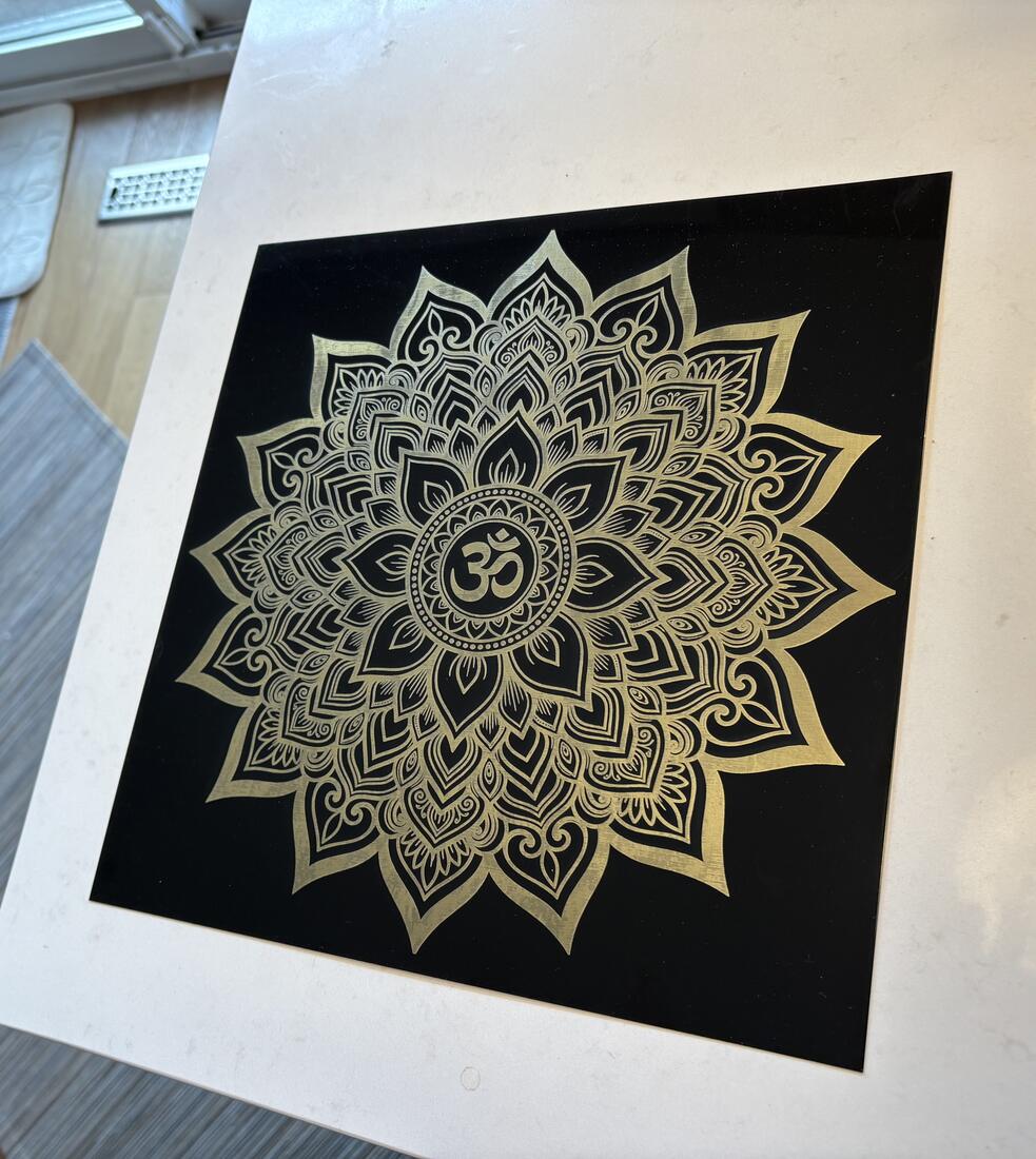 Intricate Om mandala engraved in gold on black anodized aluminum
